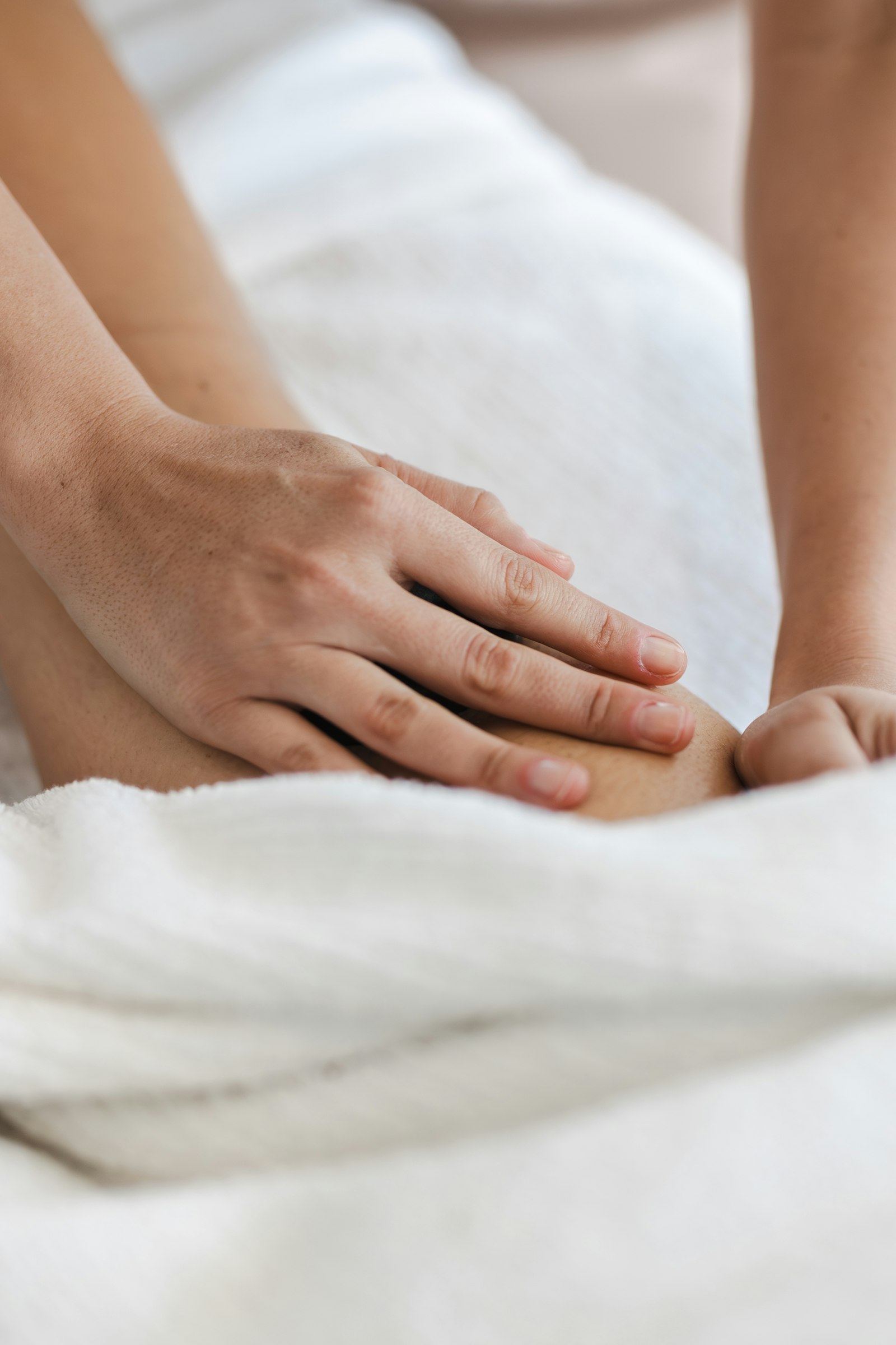 Hände massieren ein Bein auf einem weißen Handtuch