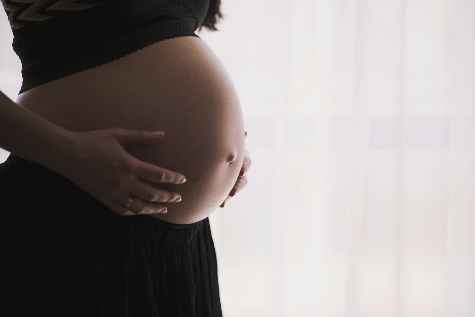 Schwangere Frau hält ihren Bauch im Gegenlicht