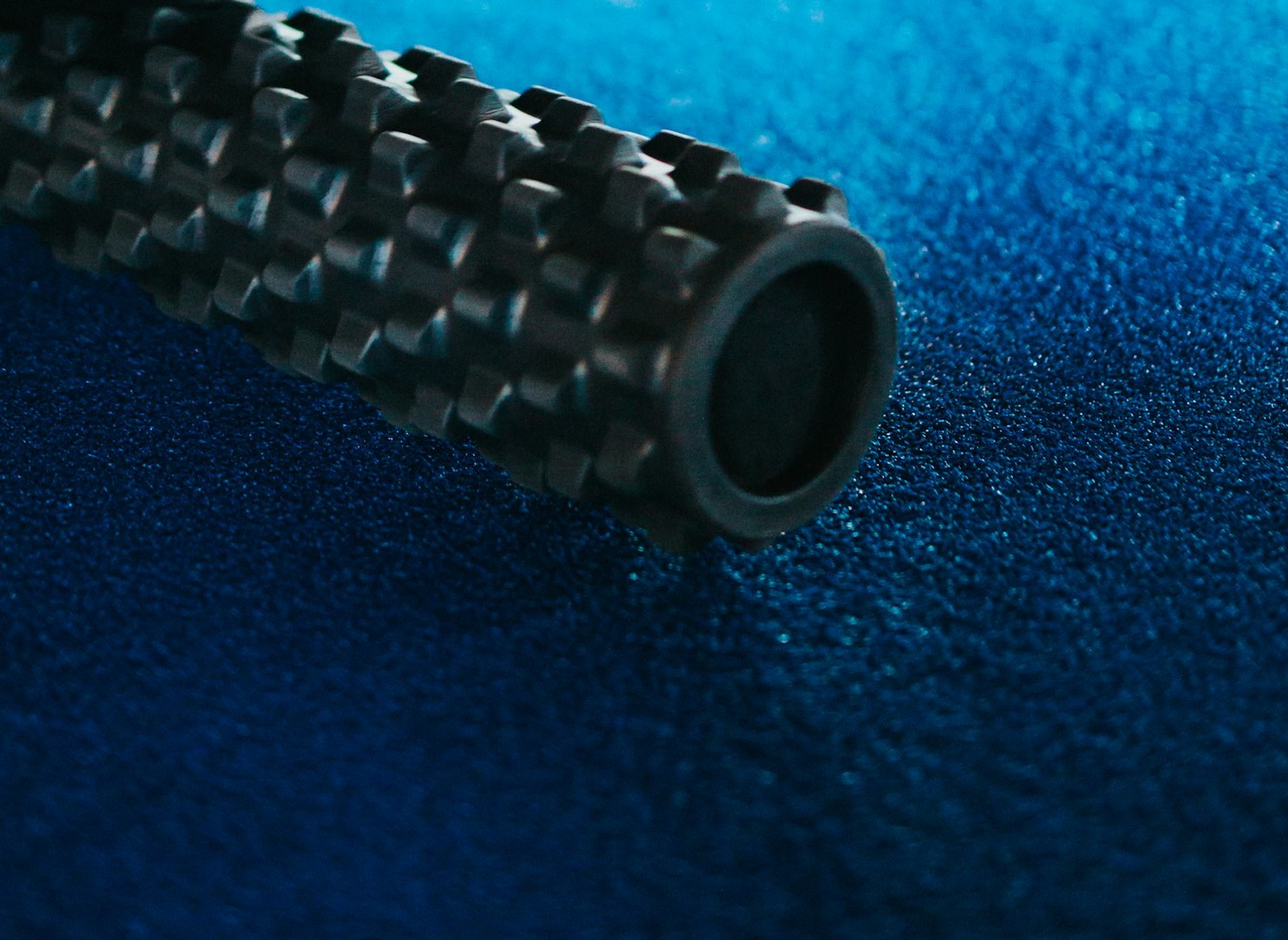 Schwarze Faszienrolle mit Noppen auf einem blauen Hallenboden